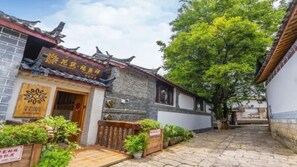 A traditional Chinese courtyard with a wooden gate, potted plants, and a signboard.
