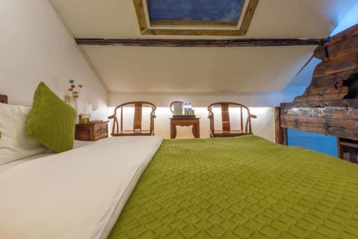Un dormitorio con tragaluz, una cama con ropa de cama verde, dos sillas de madera, una mesita de noche y un cabecero de madera.