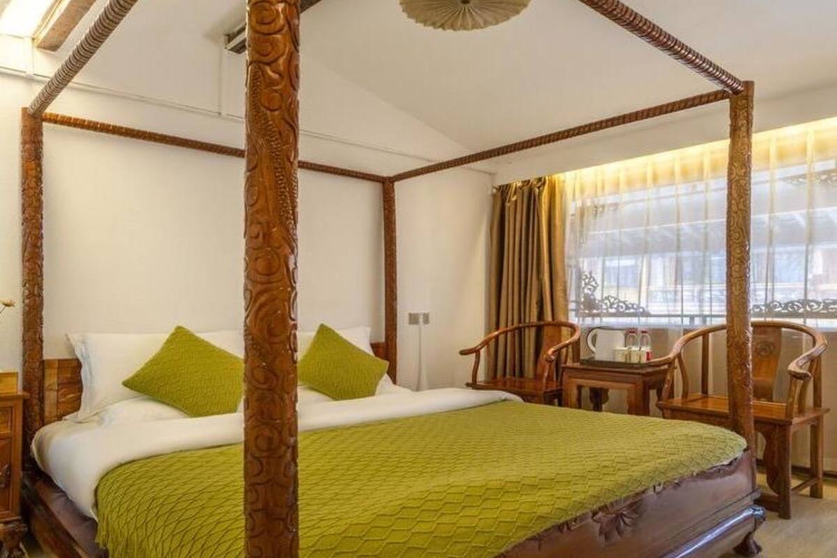 Una cama con dosel, ropa de cama verde, muebles de madera y un ventanal con cortinas.