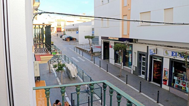 Straatbeeld met een 'Phone House' winkel, een 'El Oso Coloso' winkel en een voetpad met een groene balustrade.