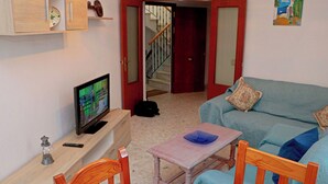 Een woonkamer met een televisie, een tafeltje, een bank en een trap naar een andere kamer.