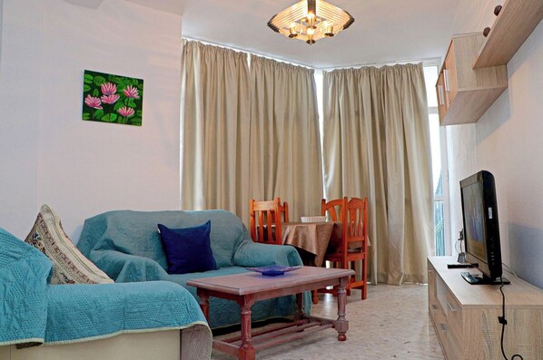 A living room with a sofa, a coffee table, a TV, and a dining table with chairs.