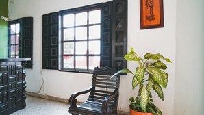 Een kamer met een houten bankje, een potplant en een raam met zwarte luiken.