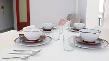 Una mesa de comedor dispuesta con cuencos, platos y vasos blancos, todo ordenado en una habitación con paredes blancas y una puerta roja.