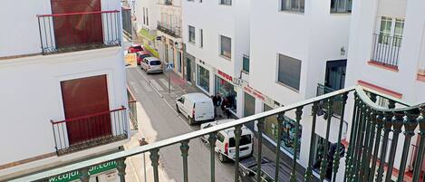 Straatbeeld met een wit gebouw met balkons, een bord met 'Hostal' en geparkeerde auto's.