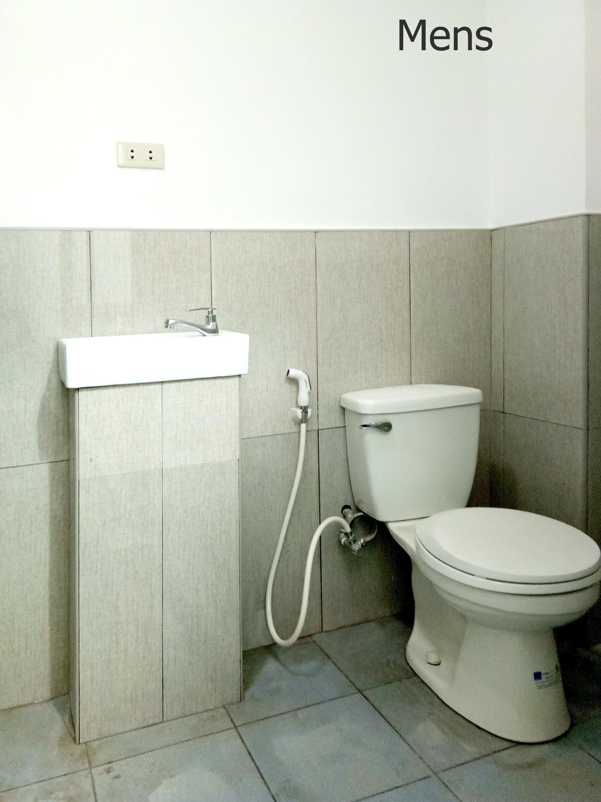 A men's bathroom with a toilet, sink, and a shower head.