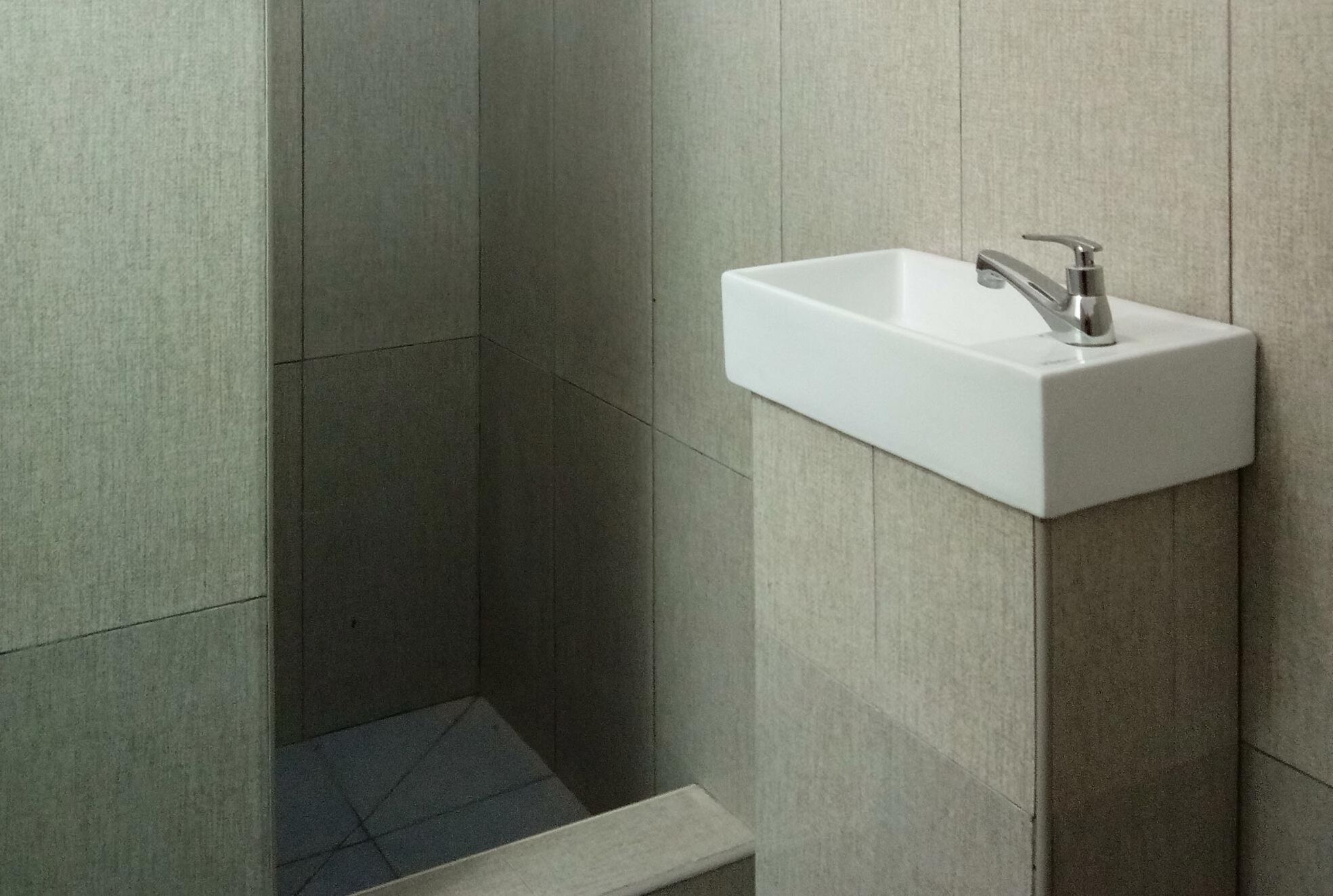 A modern bathroom with a white sink mounted on a wall, a shower area with tiled walls, and a small step leading into the shower.