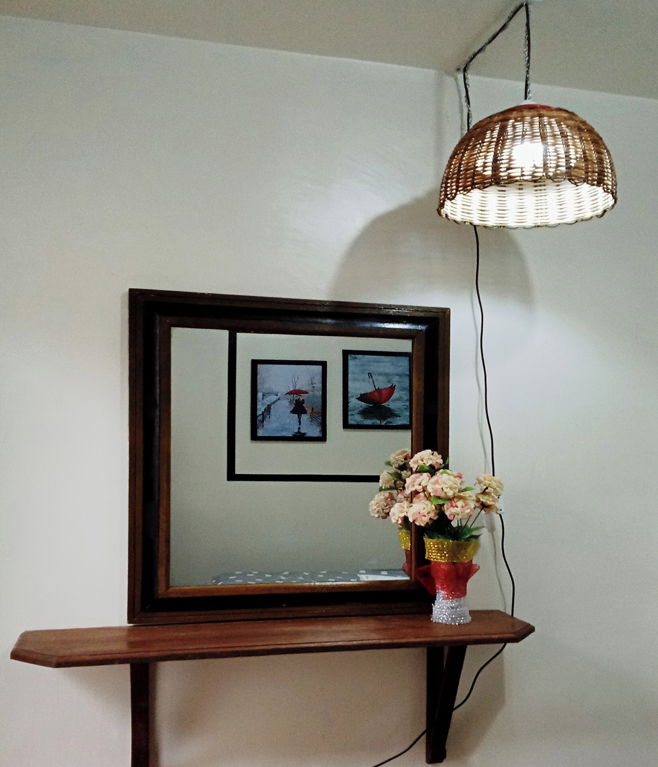 A wooden console table with a mirror above it, a hanging wicker light fixture, and a vase with flowers.