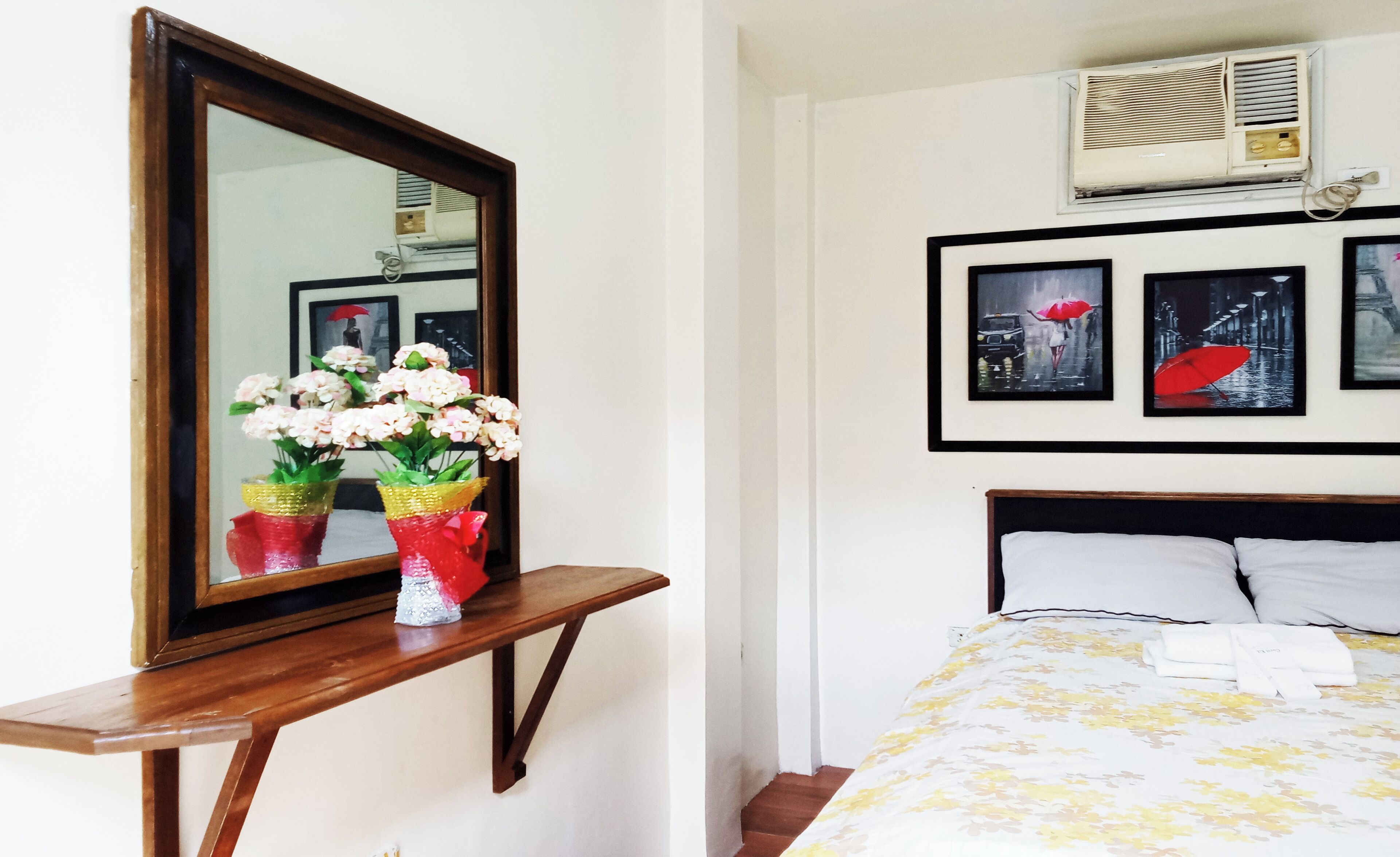 A hotel room with a bed, a nightstand with a mirror, and wall-mounted artwork.