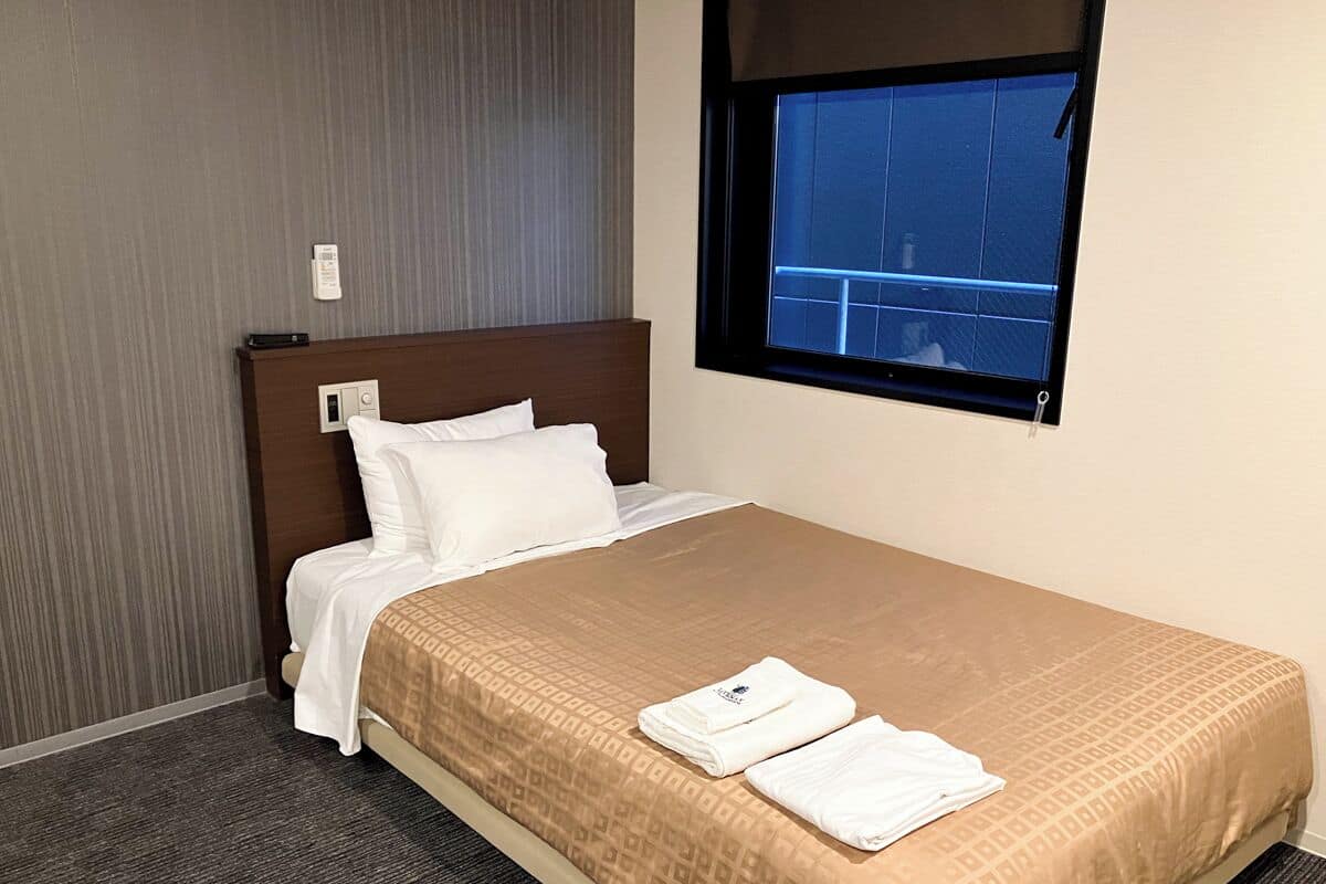 Ett hotellrum med en säng, ett fönster och en väggmonterad termostat.