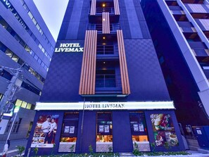 El exterior del Hotel Livemax, con un letrero llamativo, ventanas amplias y anuncios del café y café de la propiedad.