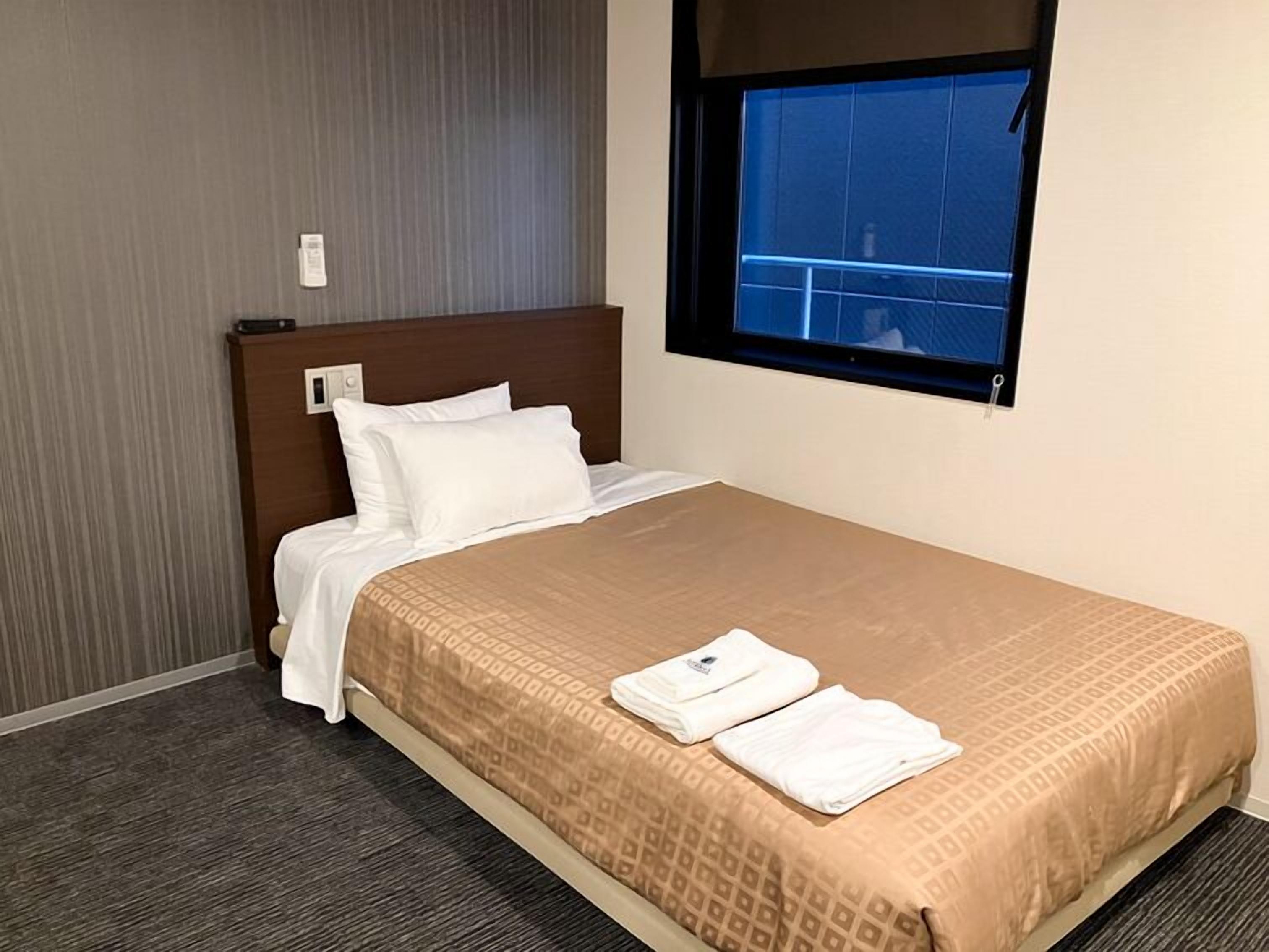 Une chambre d’hôtel avec un lit, une fenêtre donnant sur un paysage agréable, une tête de lit en bois et un panneau de commande fixé au mur.