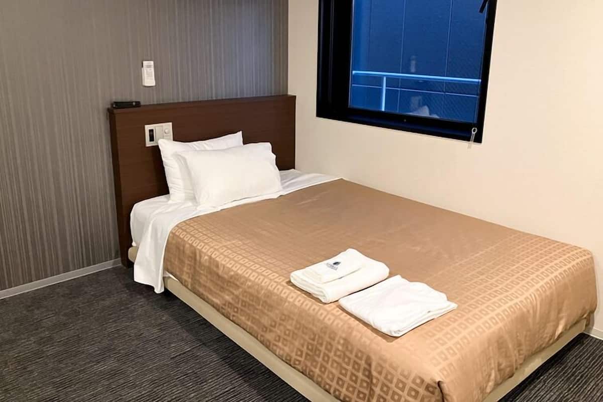 Ett hotellrum med en säng, ett fönster med utsikt, en sänggavel i trä och en väggmonterad kontrollpanel.