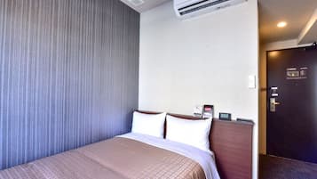 A hotel room with a bed, an air conditioning unit, a clock, and a door.
