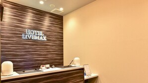 A hotel reception desk with a modern design, featuring a wooden panel wall with the hotel name, a reception counter with a computer, a phone, and a small plant. - Hotel Livemax Hakata Nakasu (Fukuoka)