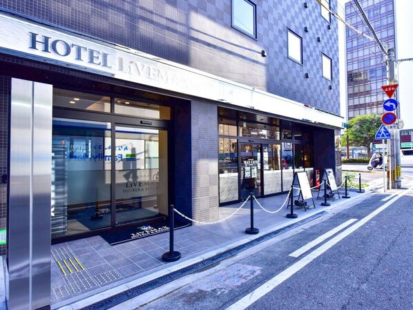 Entrada de hotel con diseño moderno, con grandes ventanales de vidrio y una puerta de metal.