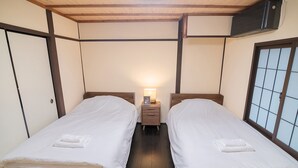 A room with two single beds, a nightstand with a lamp, and a window with a grid pattern. - Kyokoi Reishikamogawa (Kyoto)