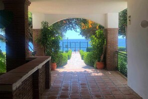 Een pad dat leidt naar een balkon met uitzicht op zee, omringd door potplanten en een bakstenen muur.