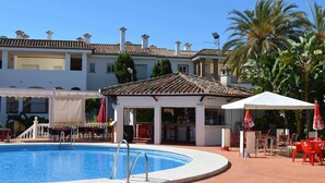 Piscina com deck revestido, mobiliário ao ar livre e área coberta com guarda-sóis.