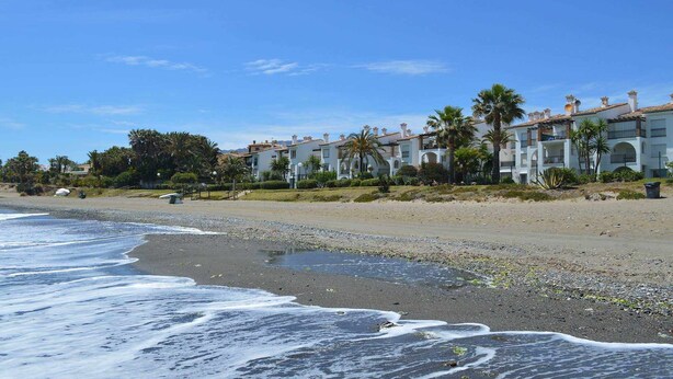 Um hotel à beira-mar com edifícios de vários andares, palmeiras e uma praia de areia.
