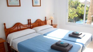 Uma cama de casal com cabeceira de madeira, duas mesas de cabeceira e uma janela com vista para árvores.