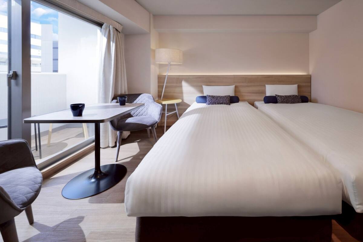 A hotel room with a large bed, a desk with a chair, a small table, and a lamp.