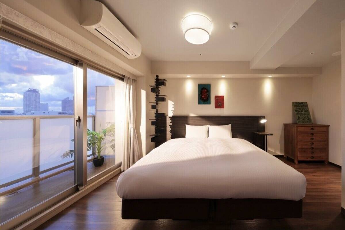 A modern hotel room with a large bed, a city view, a flat-screen TV, and a wooden dresser.