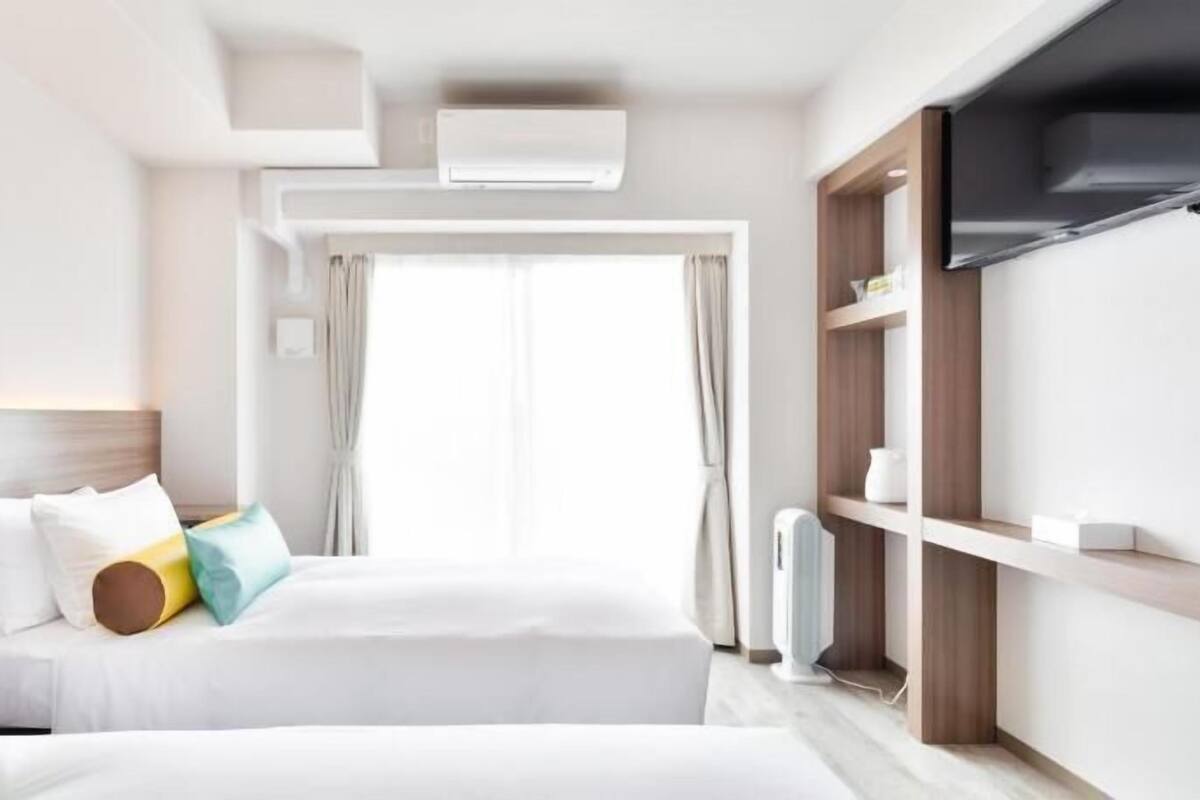 A hotel room with two beds, a TV, a wardrobe, and a window with curtains.