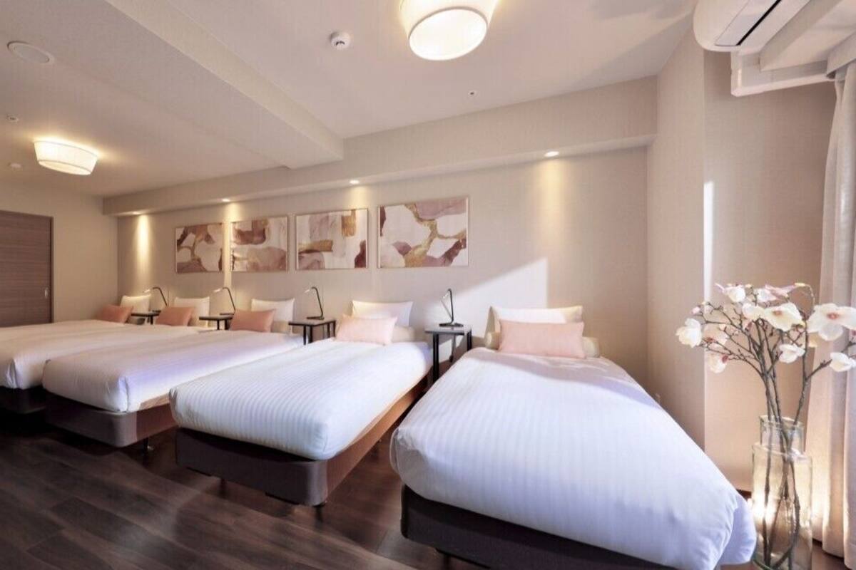 A hotel room with three beds, a desk, and a vase of flowers.