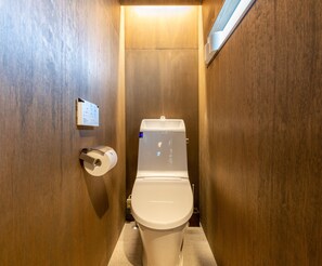 Une petite salle de bain aux finitions en bois, dotée de toilettes blanches, d’un distributeur d’essuie-tout et d’un panneau fixé au mur.