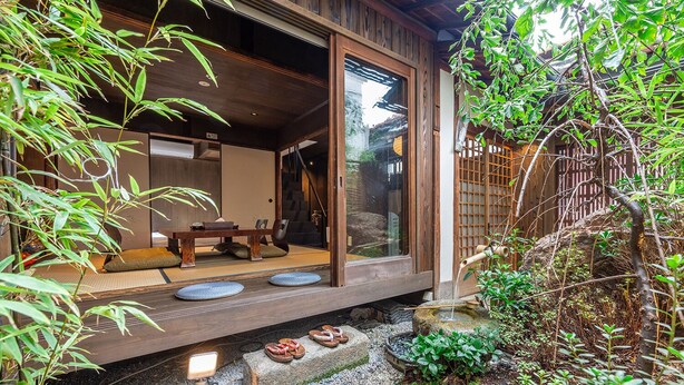 A traditional Japanese-style room with tatami flooring, a low wooden table, and a sliding door leading to a garden area with a small water feature and plants. - Kyokoi Kiyomizu (Kyoto)