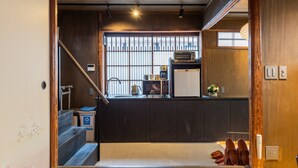 A compact kitchen with dark wooden cabinets, a built-in microwave, and a small window with bars. - Kyokoi Kiyomizu (Kyoto)