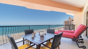 Ein Balkon mit Tisch und Stühlen, einem roten Liegestuhl und Blick auf Strand und Meer.