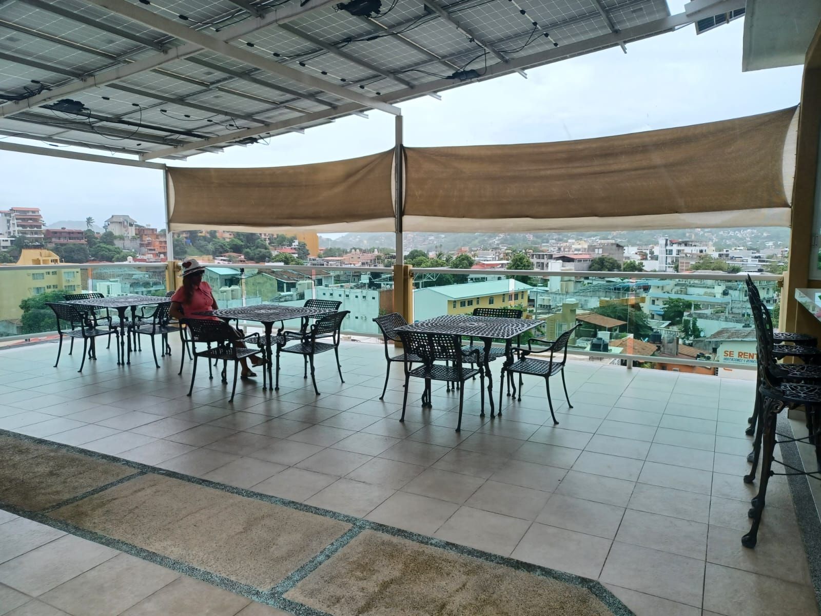 Una terraza exterior con una mesa y sillas, una persona sentada, y vista a la ciudad.