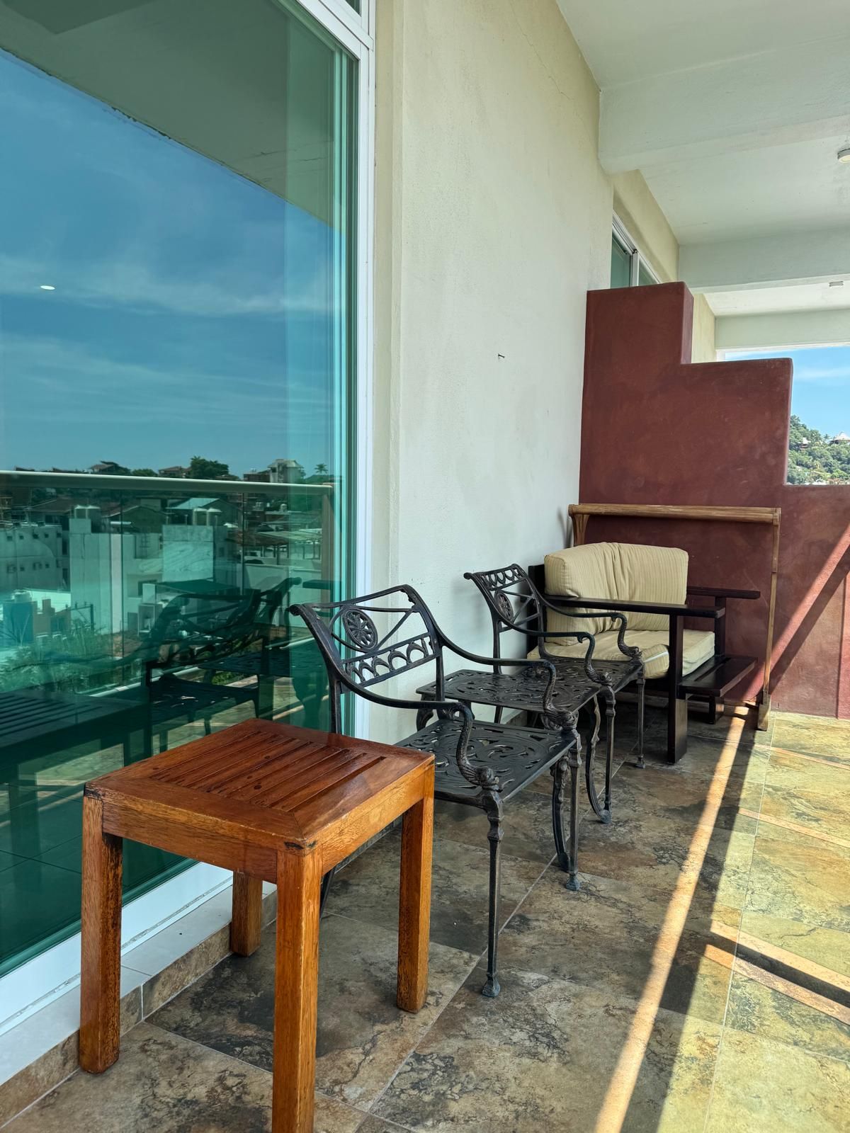 Un balcon avec une table et des chaises en bois, une paroi en verre et une vue sur la ville.