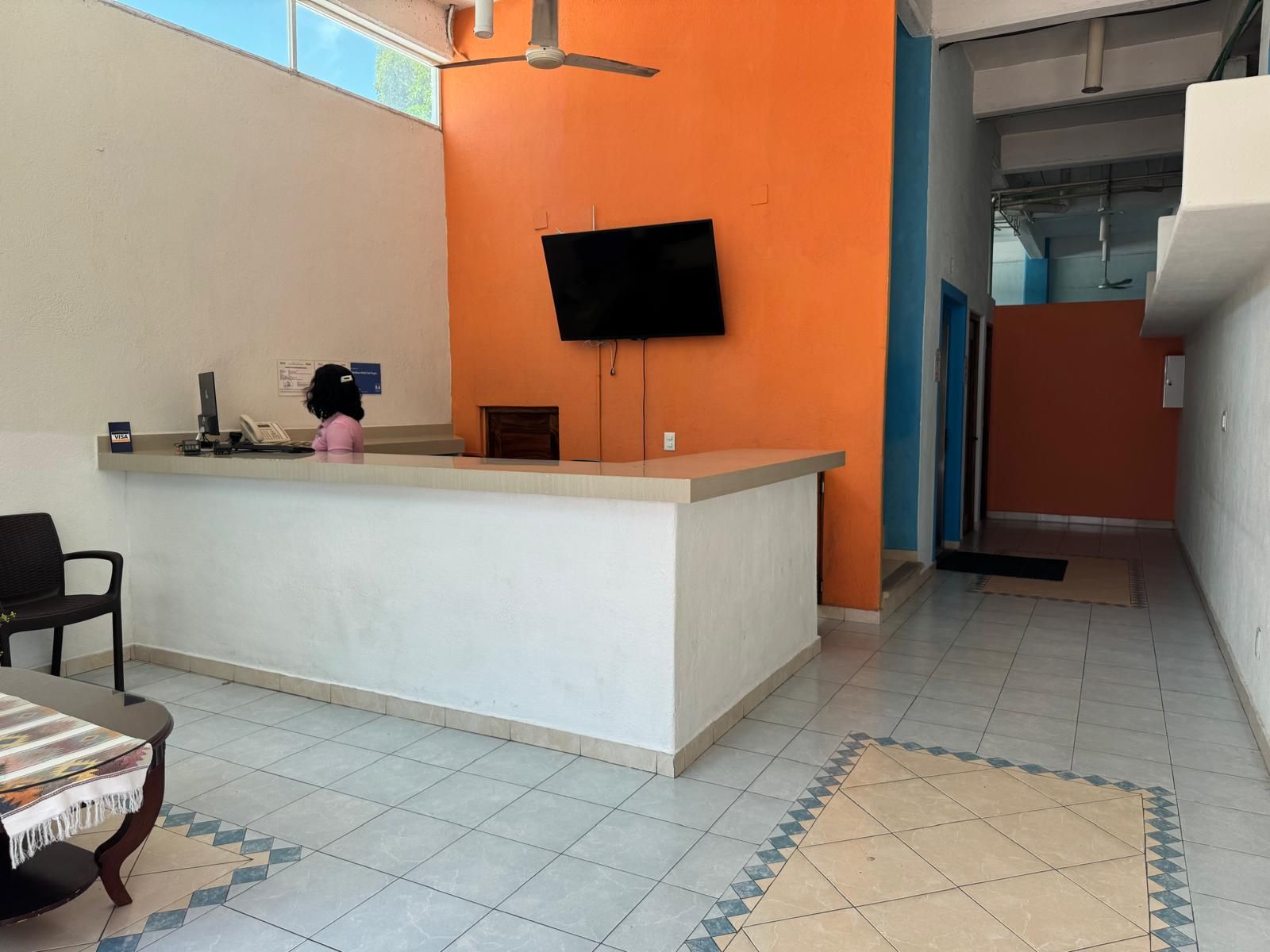 A reception area with a flat-screen TV mounted on the wall, a reception desk, a chair, and a patterned rug.
