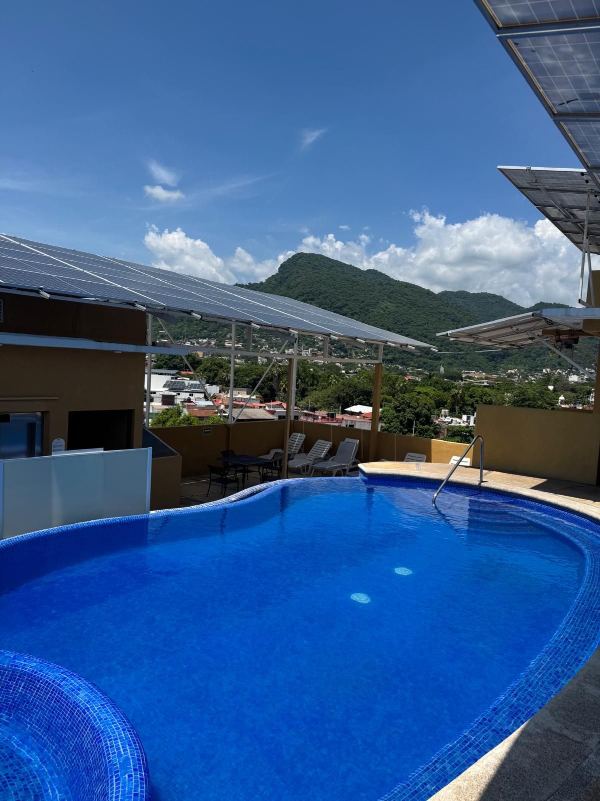 Una piscina con vistas a una montaña y paneles solares al fondo.