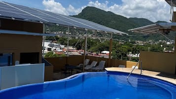 Una piscina con vistas a una montaña y paneles solares al fondo.