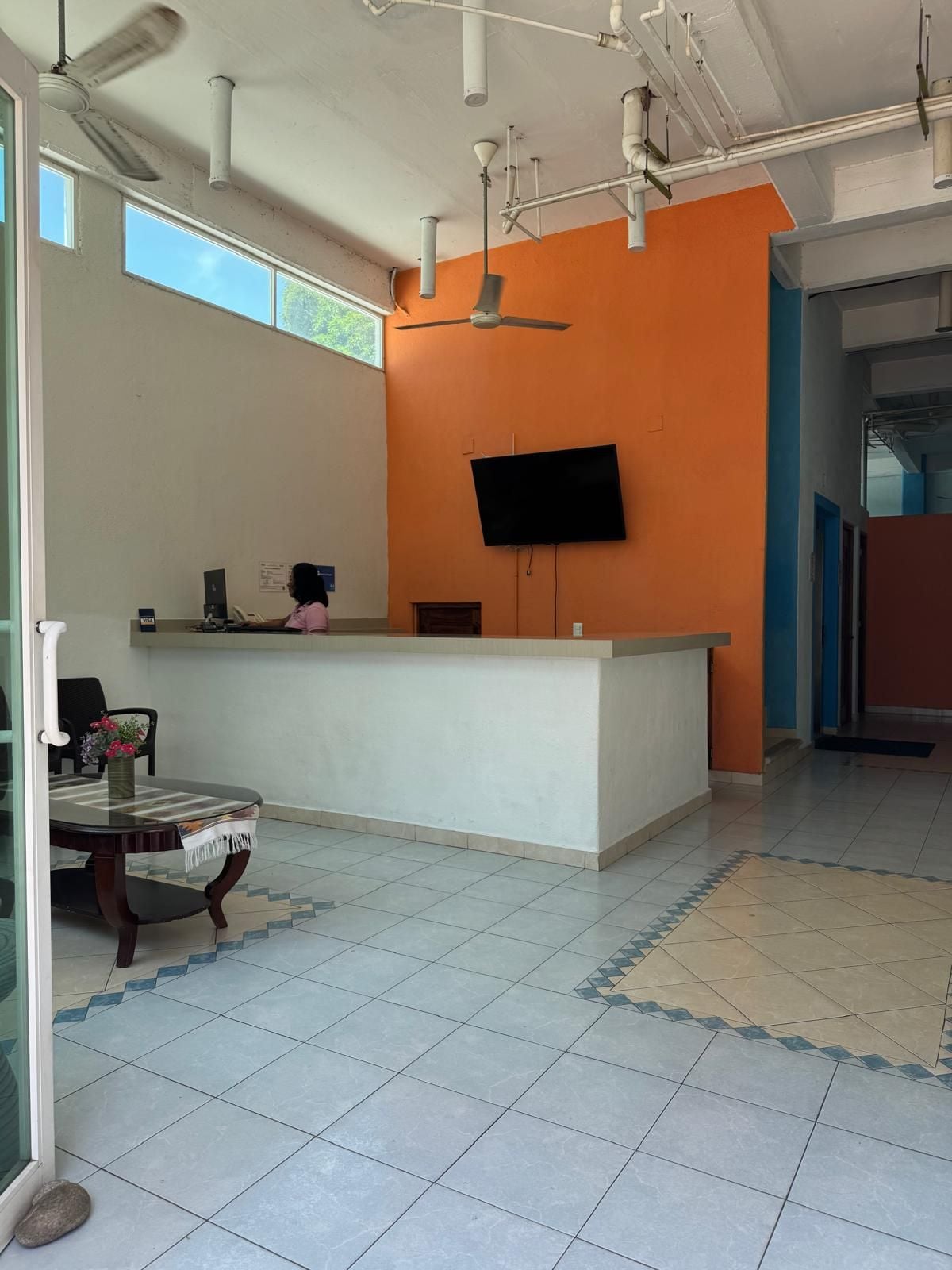A reception area with a flat-screen TV mounted on the wall, a reception desk, and a seating area with a table and chairs.