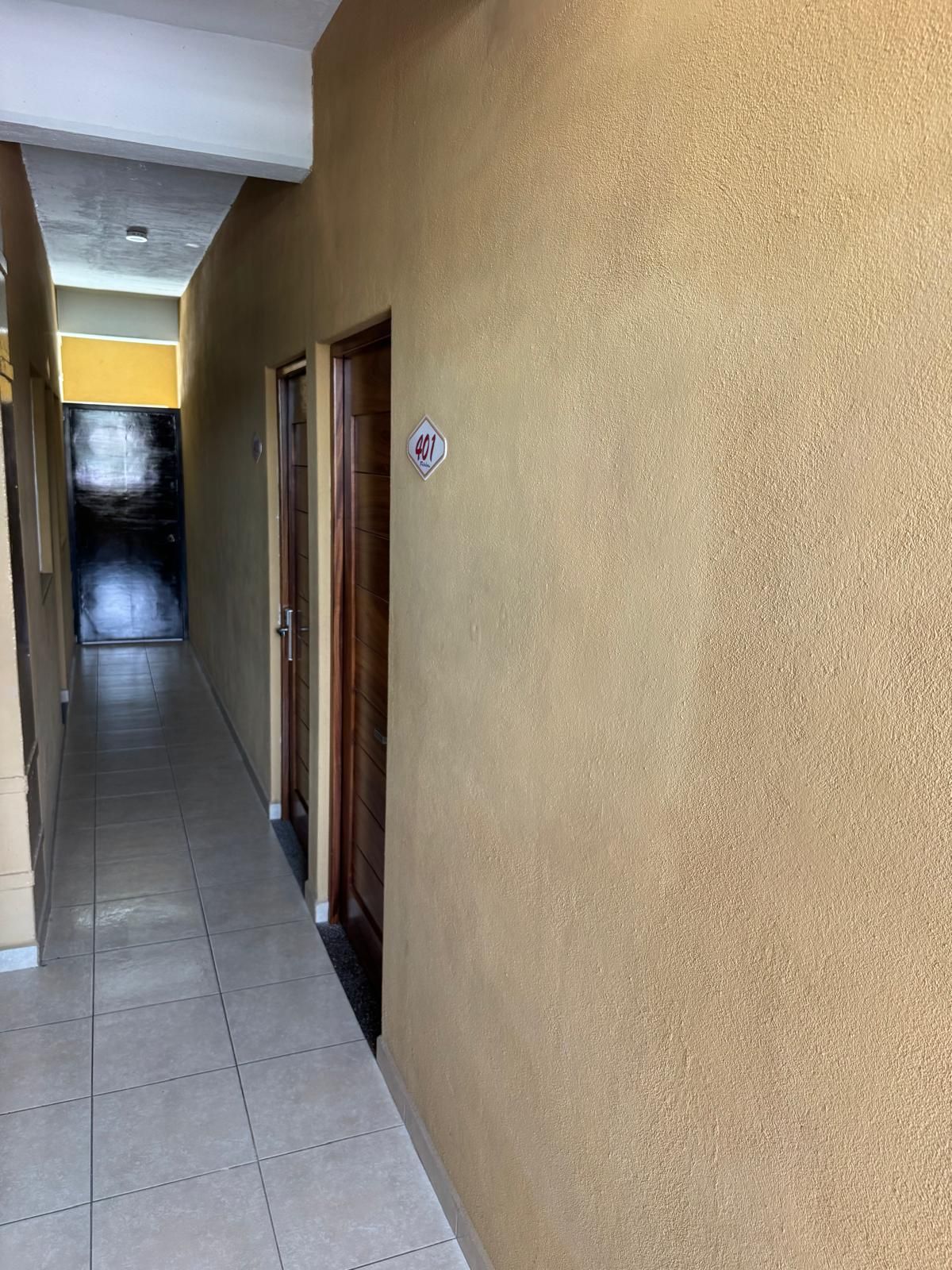 A corridor with a tiled floor, beige walls, and doors on the right.