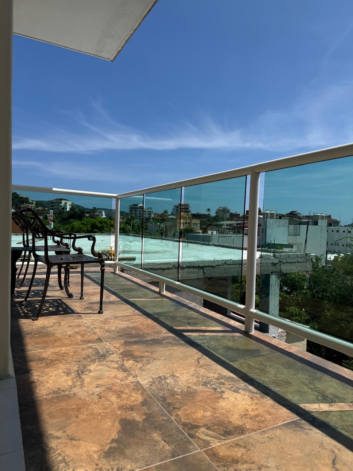 Ein Balkon mit Glastrennwand, Sitzgelegenheit im Freien und Blick auf eine Stadtlandschaft.