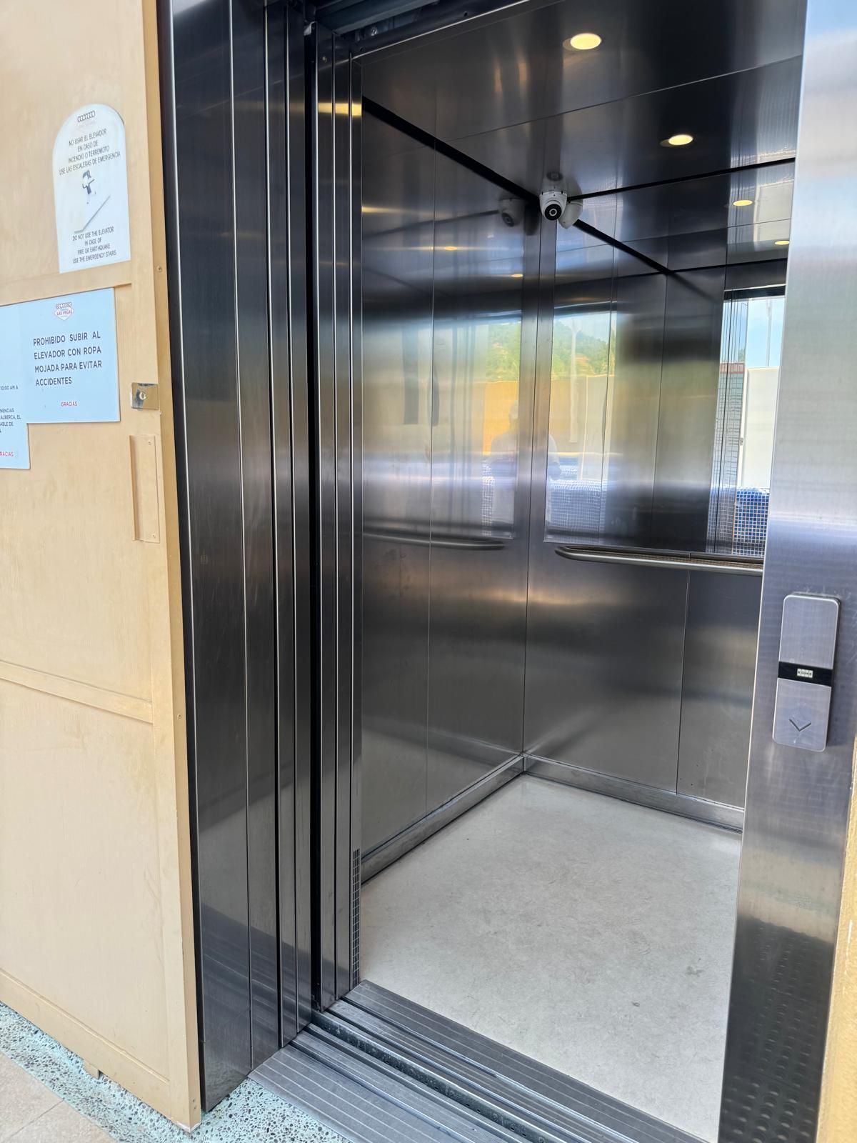 An elevator with metallic doors, a security camera, and a floor indicator.