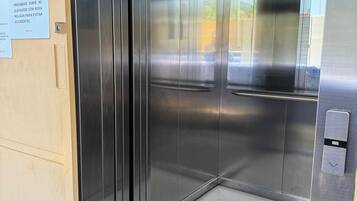 An elevator with metallic doors, a security camera, and a floor indicator.