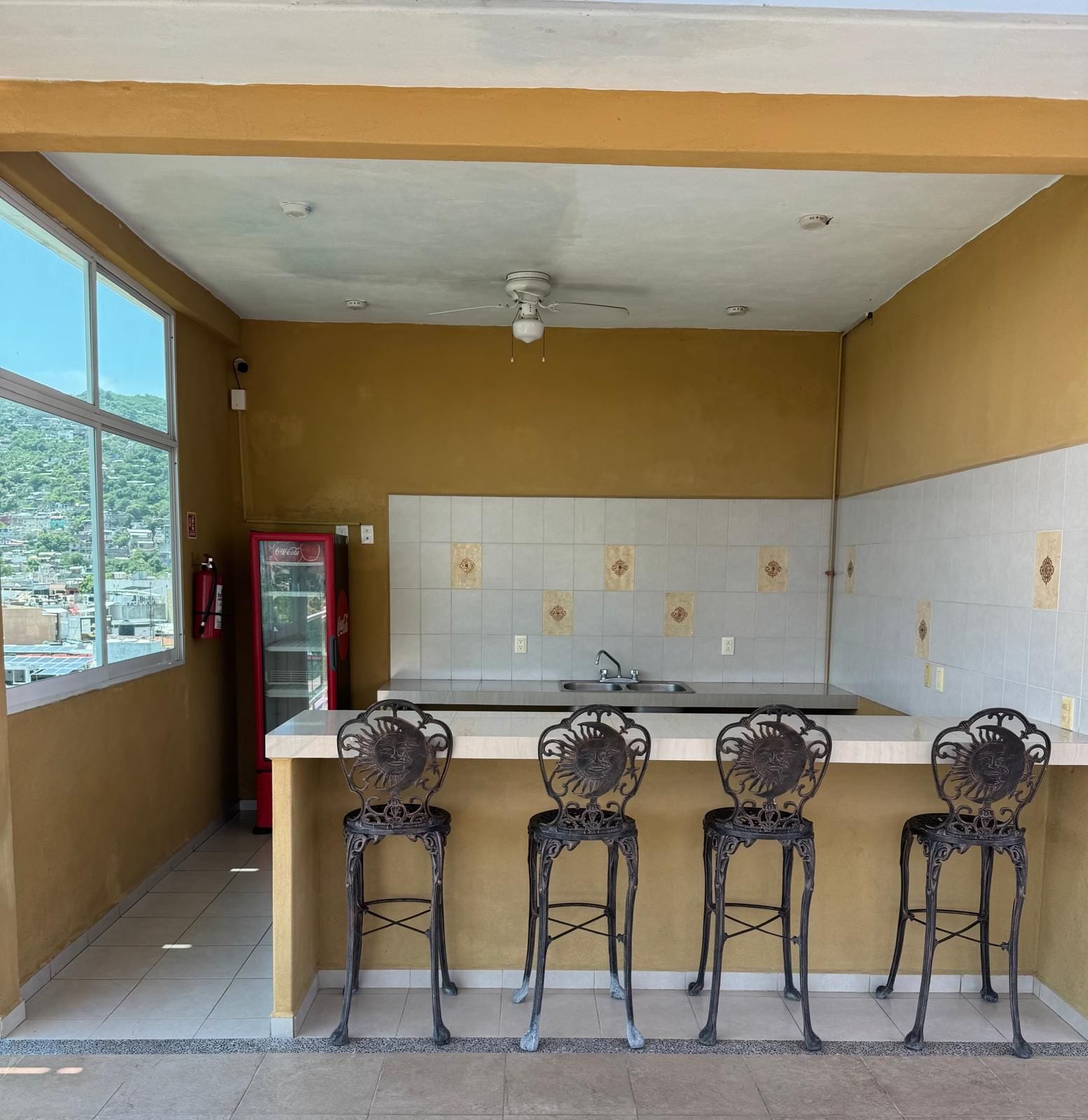 A kitchen with a white countertop, a sink, and four ornate chairs with sun motifs.
