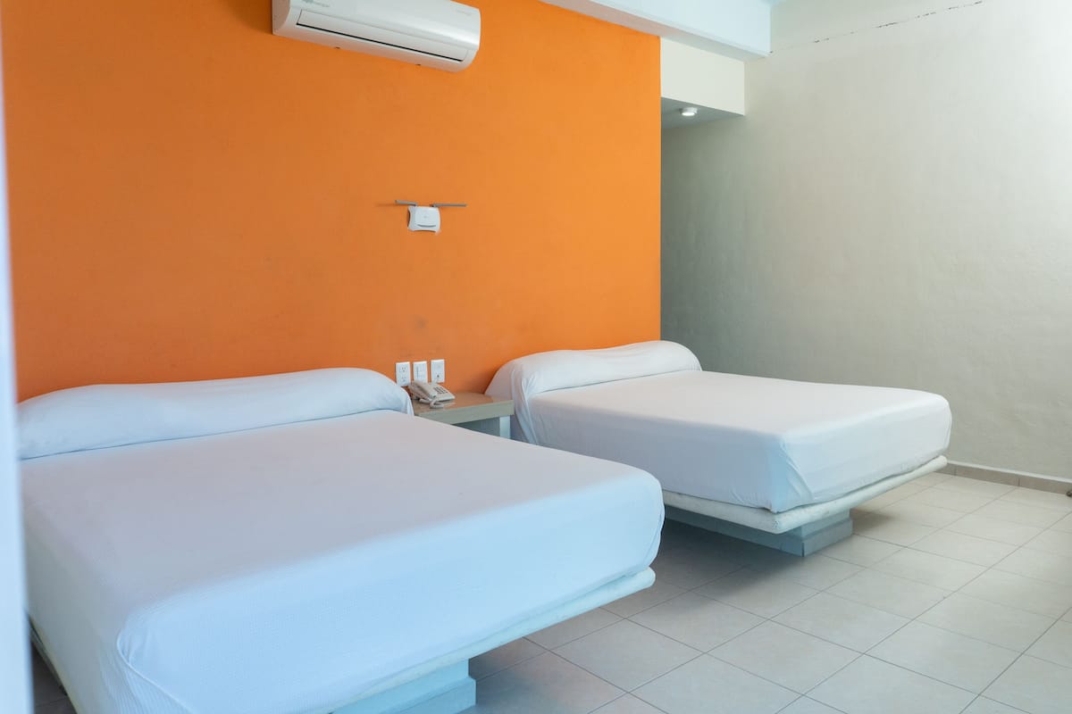 A hotel room with two single beds, an air conditioning unit, a telephone, and a small table.