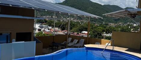 Una piscina con vistas a una montaña y paneles solares al fondo.