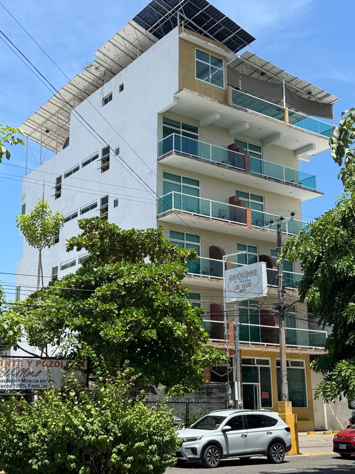 Un hôtel à plusieurs étages doté de balcons, une enseigne indiquant qu’il se trouve à Las Vegas, et une voiture blanche garée devant.