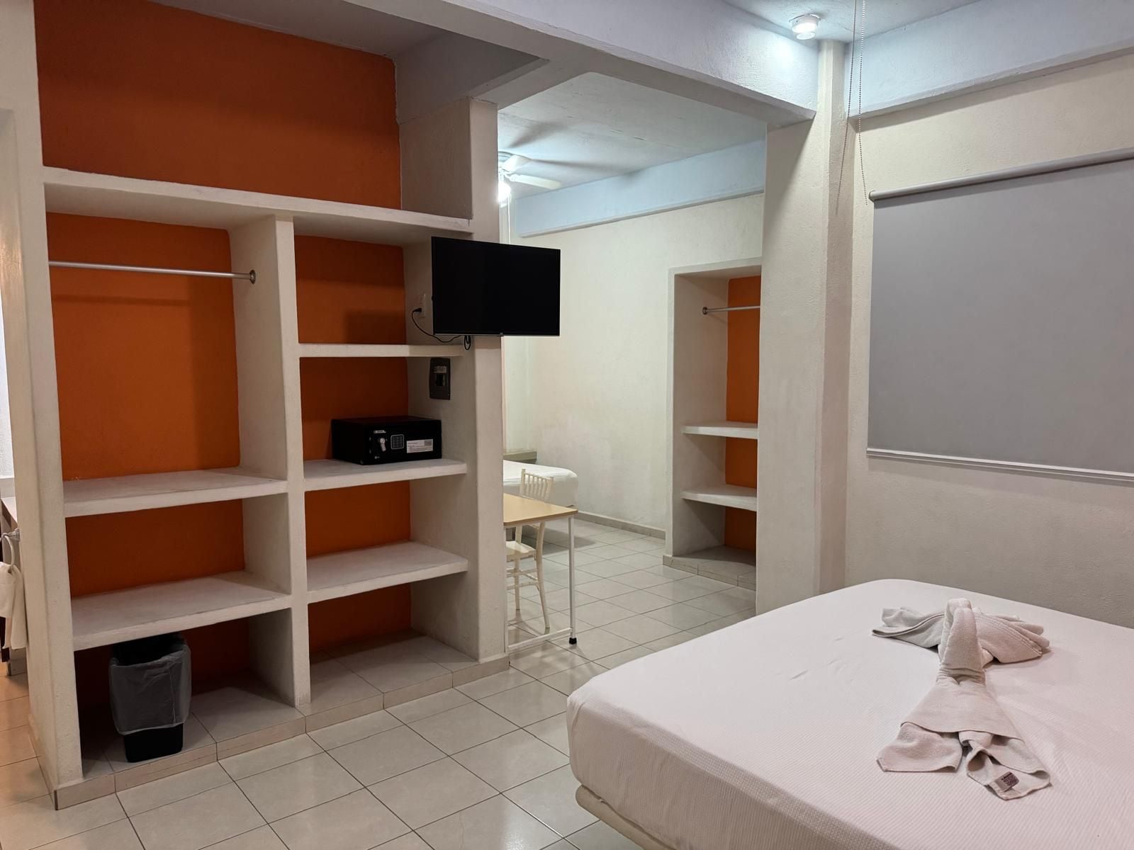 A bedroom with a bed, a TV mounted on the wall, and a wardrobe with orange shelving.