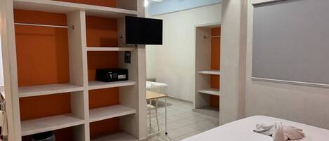 A bedroom with a bed, a TV mounted on the wall, and a wardrobe with orange shelving.