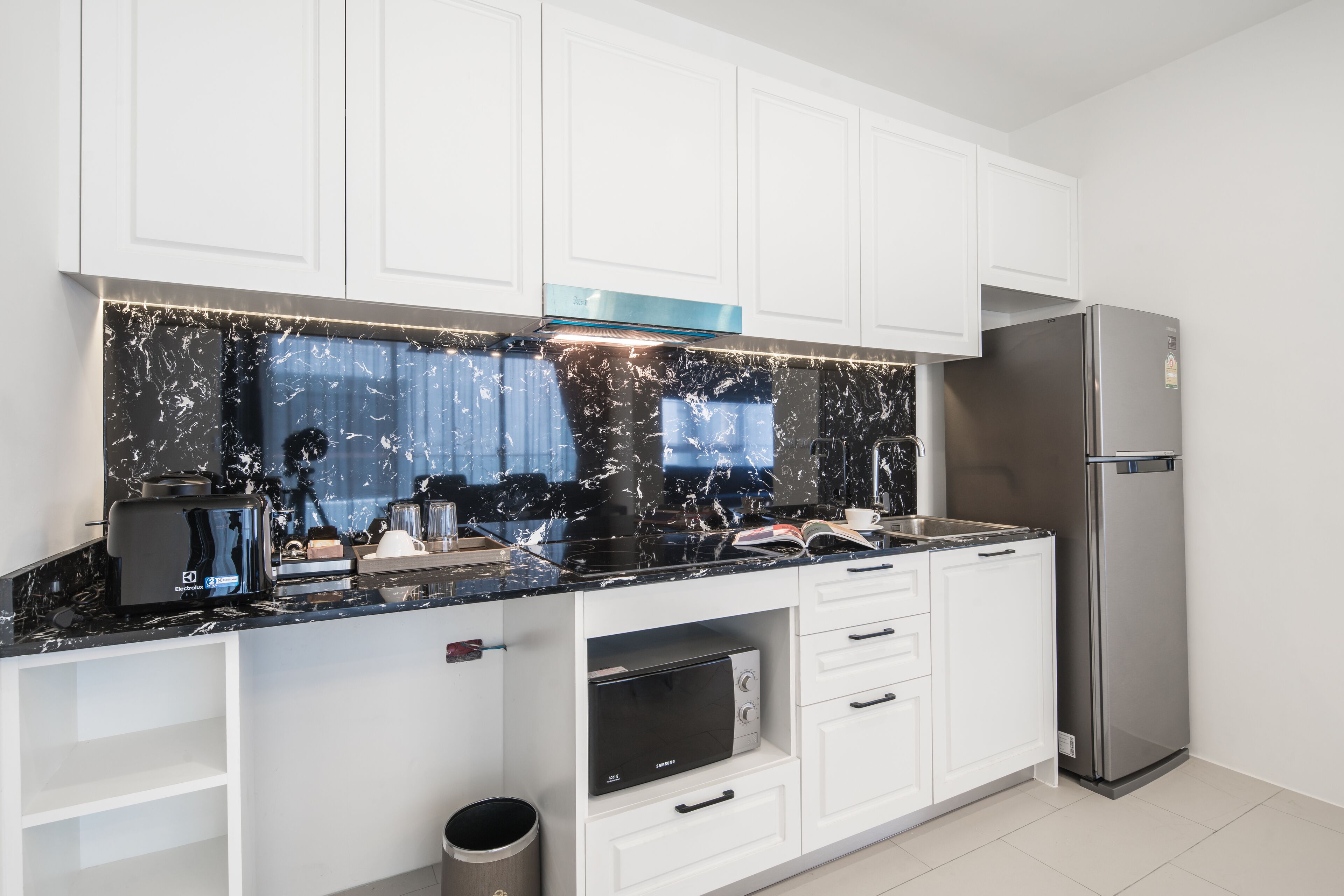 A modern kitchen with white cabinets, a black marble backsplash, a built-in microwave, and a stainless steel refrigerator.